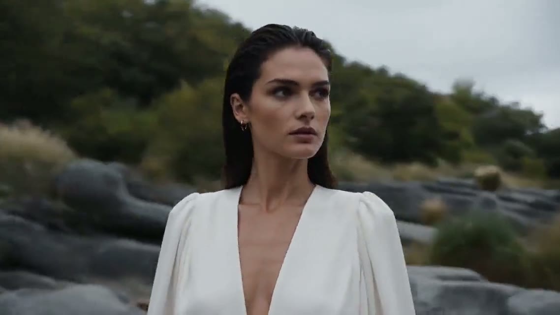 Last frame: close-up of a woman in a white blouse standing by a rocky stream.